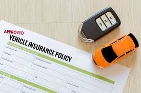 Vehicle insurance policy document with car key and toy car on a wooden surface.