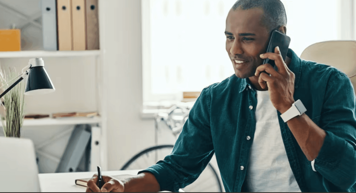 Man in a blue shirt talking on the phone while working at a desk in an office setting.